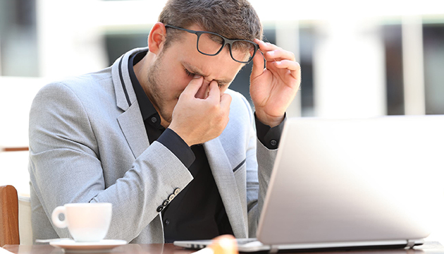 Man met pijn aan zijn ogen achter zijn laptop